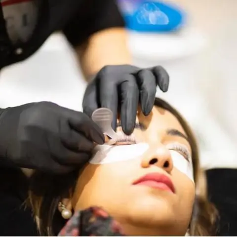 Pose d’extensions de cils sur une cliente, patch sous l’œil et pince de précision