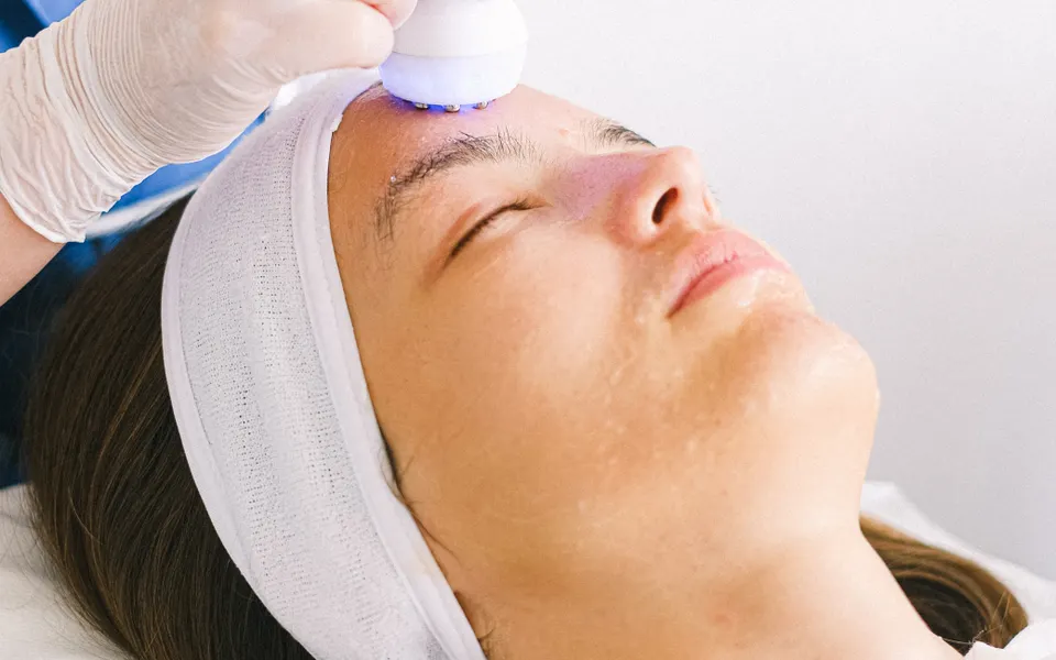 Tête de traitement à ultrasons appliquée sur le front d’une cliente allongée en cabine