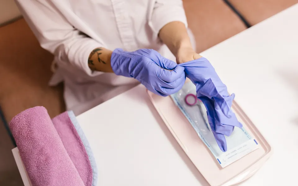 Esthéticienne enfilant des gants au-dessus d’un sachet de stérilisation posé sur un plateau