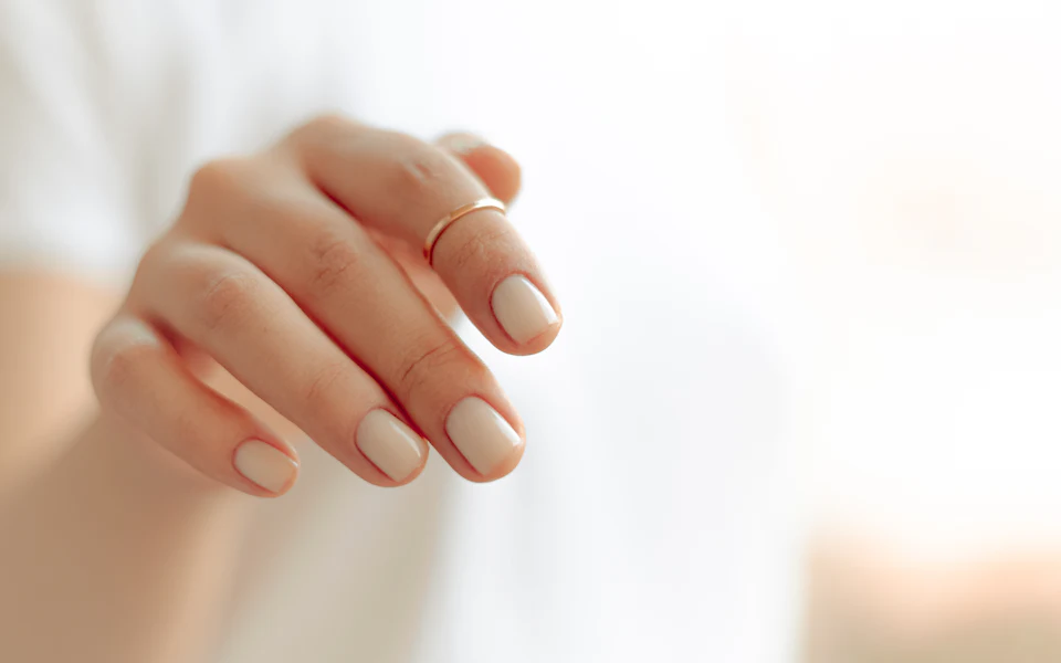 Main avec une manucure nude parfaitement limée et brillante