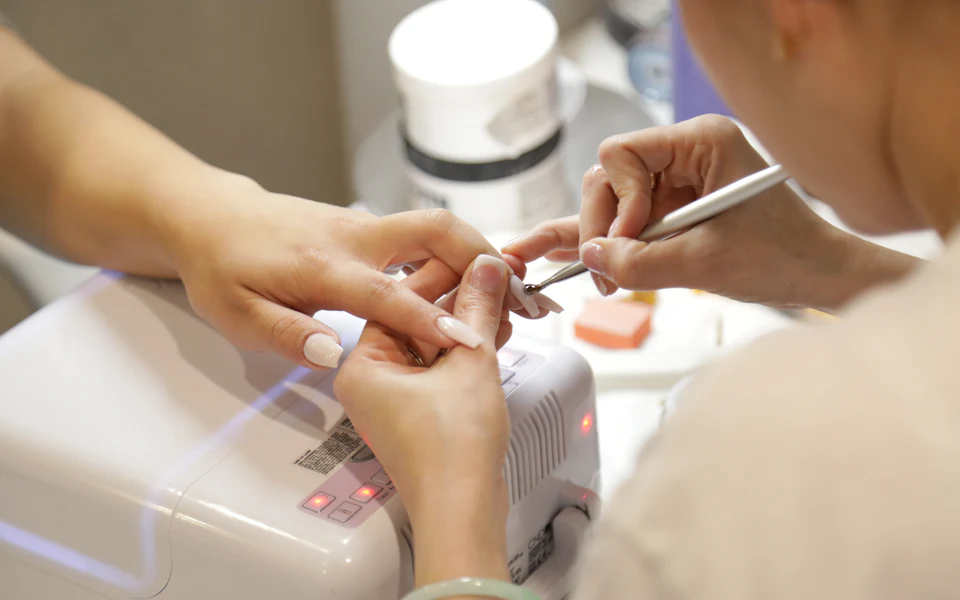 Prothésiste ongulaire réalisant une pose d’ongles en gel sur la main d’une cliente